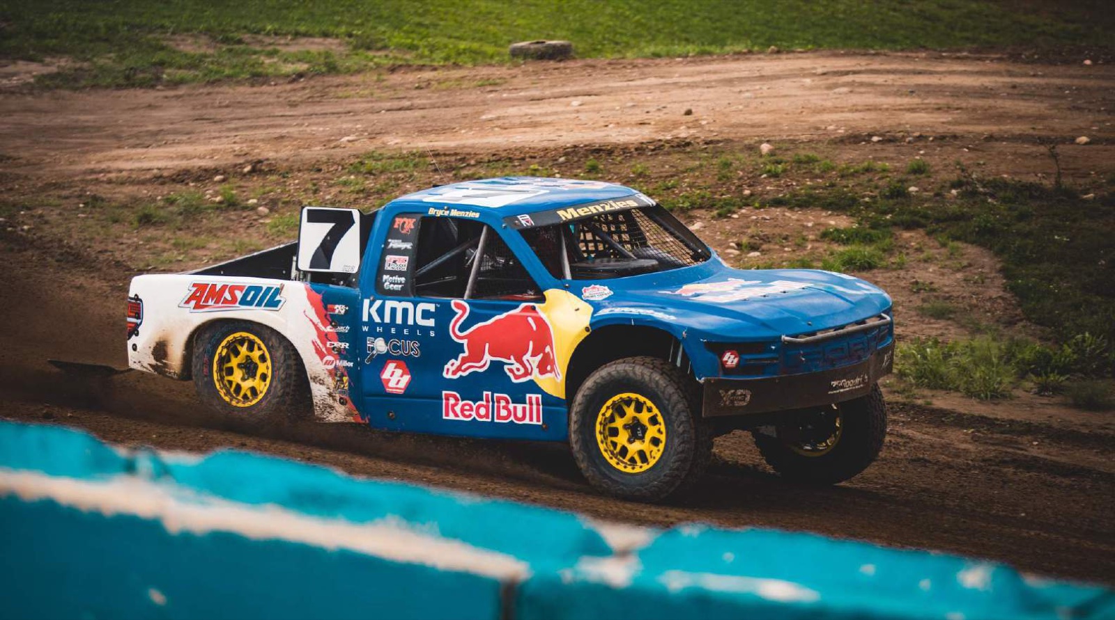 A number 7 trophy truck in blue livery running on a dirt short course